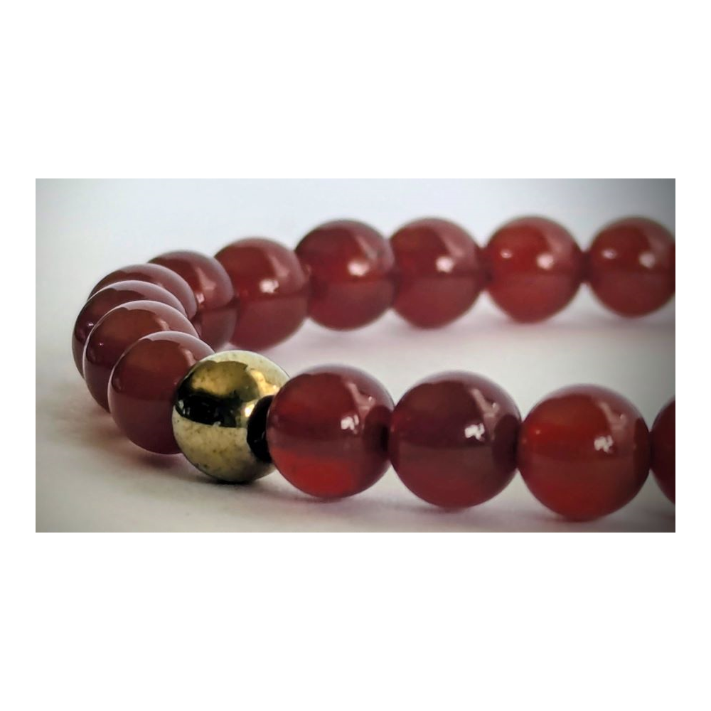 A close-up of a beaded strand with glossy round red beads and one metallic gold accent bead on a light gray background.
